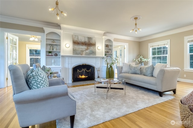 living room with a notable chandelier, light hardwood / wood-style floors, ornamental molding, and built in shelves