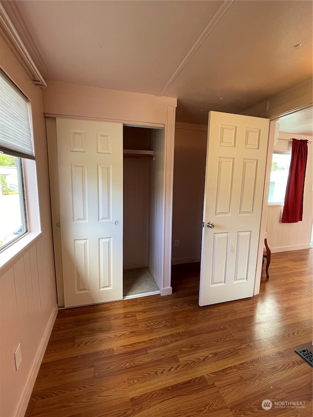 unfurnished bedroom with wood-type flooring, a closet, multiple windows, and wood walls