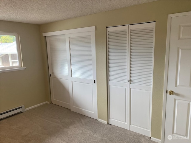 unfurnished bedroom with baseboard heating, multiple closets, light carpet, and a textured ceiling