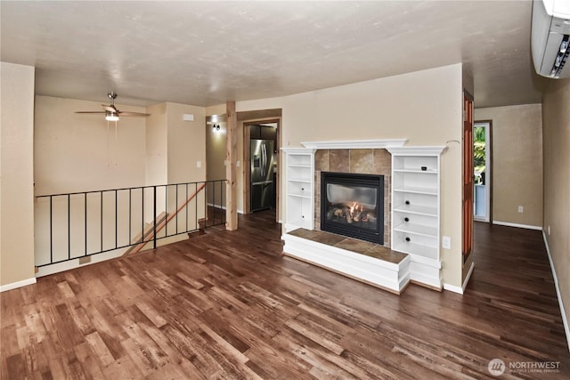 unfurnished living room with baseboards, a wall unit AC, dark wood finished floors, and a tiled fireplace