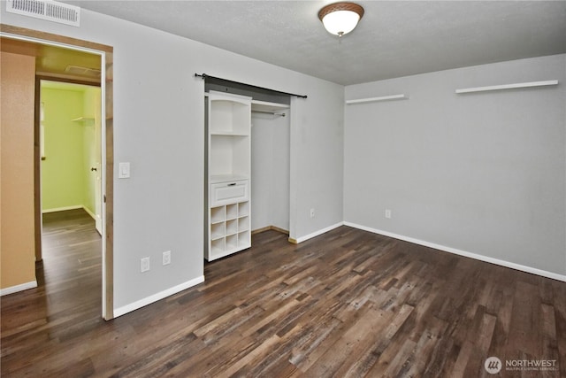 unfurnished bedroom with dark wood-type flooring, a closet, visible vents, and baseboards