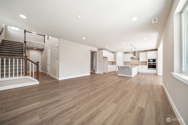 unfurnished living room with recessed lighting, visible vents, light wood finished floors, and stairs