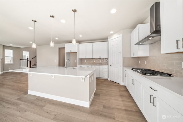 kitchen featuring wall chimney exhaust hood, light wood-style floors, a sink, and stainless steel gas stovetop