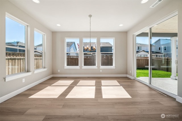 unfurnished dining area featuring wood finished floors, visible vents, baseboards, and an inviting chandelier