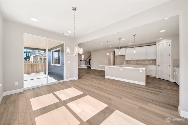 unfurnished living room featuring baseboards, visible vents, stairway, light wood-type flooring, and a sink