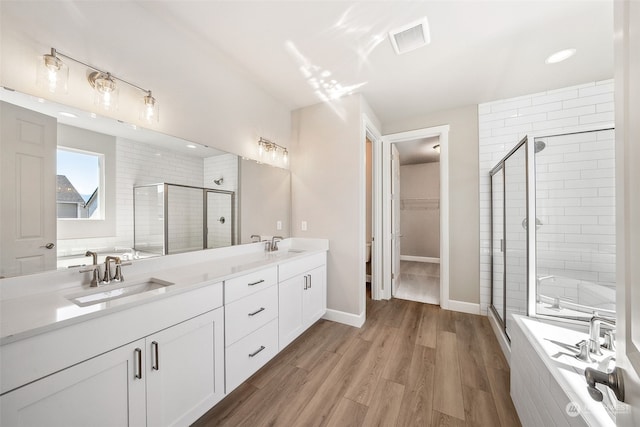 bathroom featuring double vanity, visible vents, a stall shower, a sink, and wood finished floors