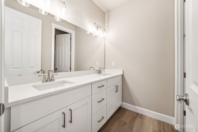 full bath with double vanity, baseboards, a sink, and wood finished floors