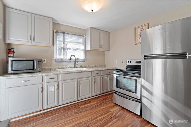 kitchen with light stone counters, stainless steel appliances, light hardwood / wood-style flooring, and sink