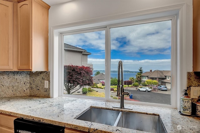 kitchen with light stone countertops, light brown cabinetry, backsplash, sink, and dishwasher