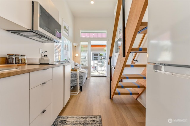 kitchen featuring stainless steel microwave, light wood-type flooring, freestanding refrigerator, white cabinets, and modern cabinets