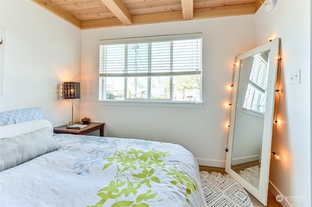 bedroom with baseboards, wooden ceiling, beam ceiling, and wood finished floors