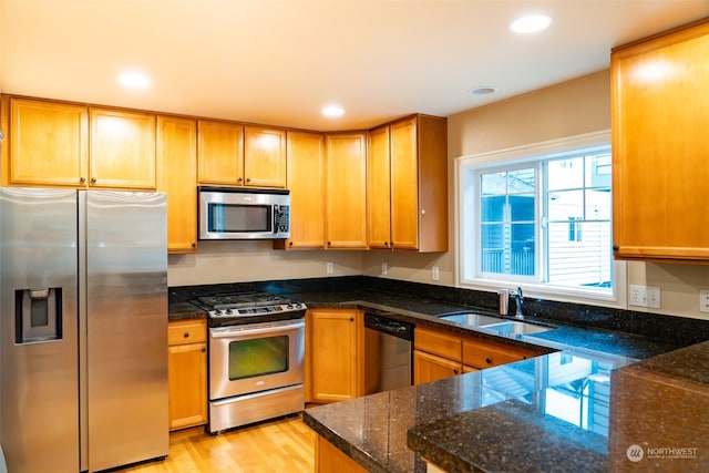 kitchen featuring appliances with stainless steel finishes, sink, dark stone countertops, and light wood-type flooring