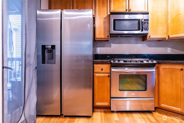 kitchen with dark stone counters, stainless steel appliances, and light hardwood / wood-style floors