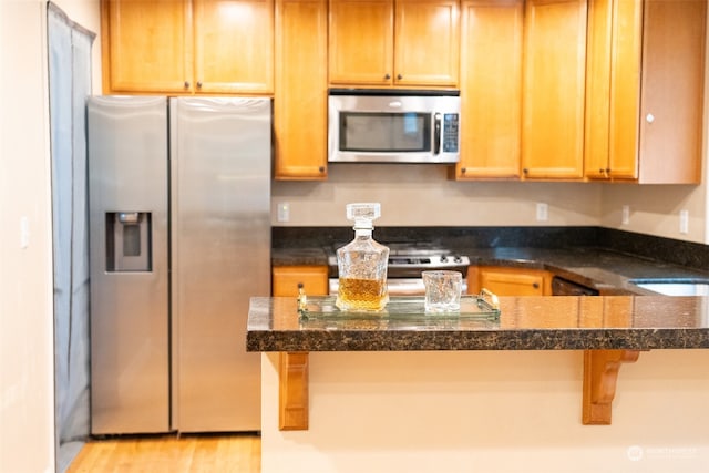 kitchen with appliances with stainless steel finishes, light hardwood / wood-style floors, a kitchen breakfast bar, and dark stone countertops