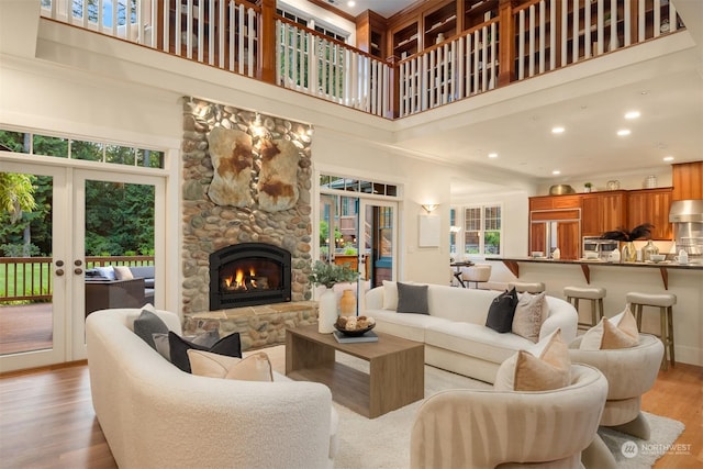 living room with a stone fireplace, light hardwood / wood-style flooring, a towering ceiling, and french doors