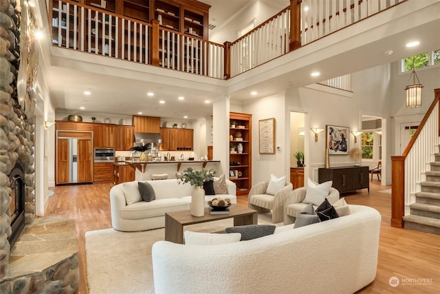 living room with a stone fireplace, light wood-type flooring, and a high ceiling