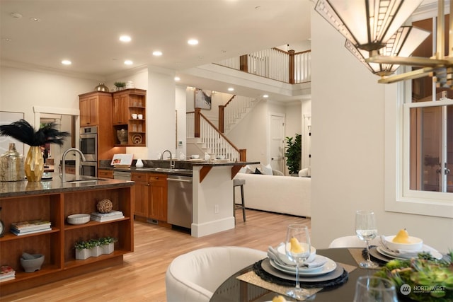 kitchen with a kitchen breakfast bar, ornamental molding, stainless steel appliances, and light hardwood / wood-style flooring