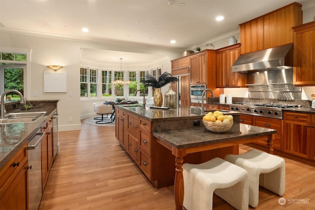 kitchen featuring appliances with stainless steel finishes, wall chimney exhaust hood, a breakfast bar, a kitchen island with sink, and sink