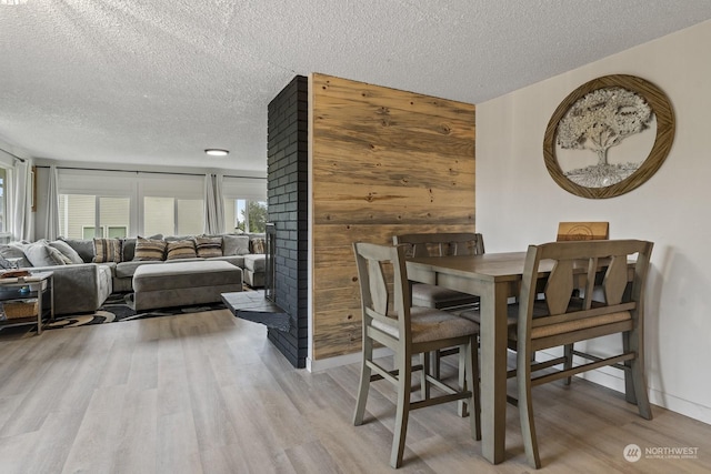 dining room featuring wood walls, a textured ceiling, and light hardwood / wood-style flooring