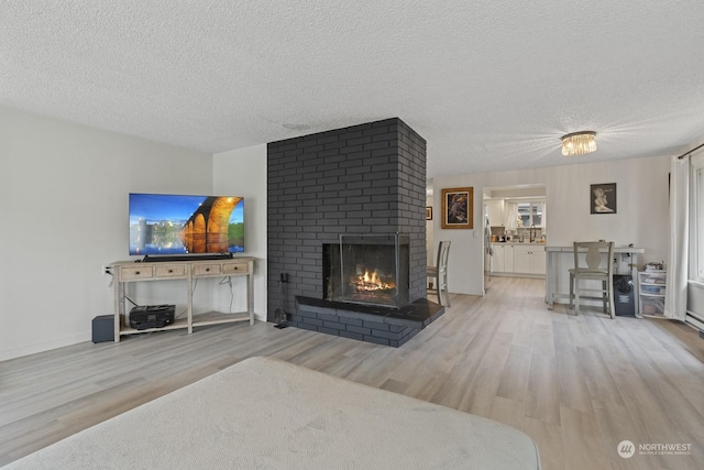 living room with light hardwood / wood-style flooring, a textured ceiling, and a brick fireplace