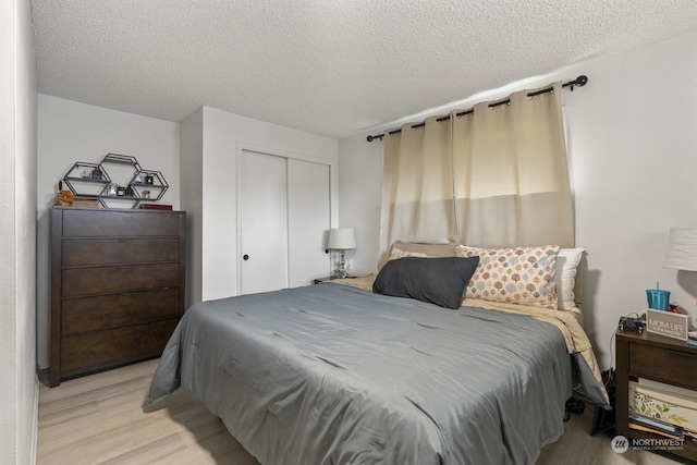 bedroom with light wood-type flooring, a textured ceiling, and a closet