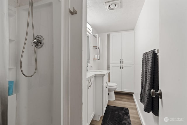 bathroom featuring vanity, a textured ceiling, a shower, wood-type flooring, and toilet