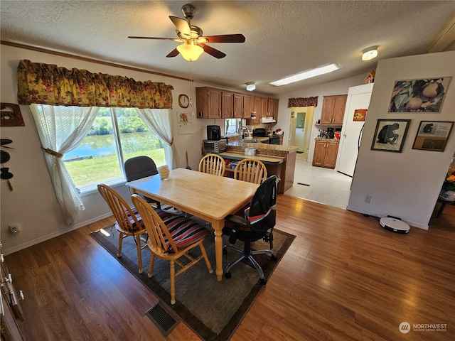 dining area with a textured ceiling, lofted ceiling, light hardwood / wood-style flooring, sink, and ceiling fan