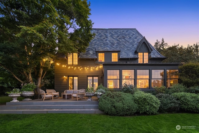 back house at dusk featuring a lawn, an outdoor living space, and a patio