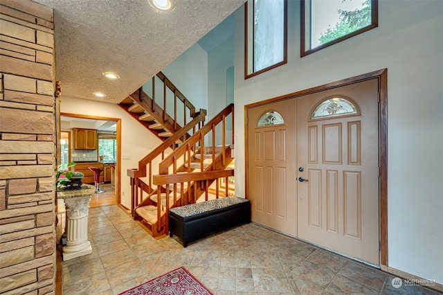 entrance foyer with a wealth of natural light, tile flooring, a high ceiling, and a textured ceiling