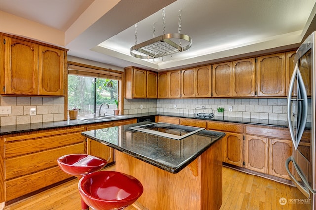 kitchen featuring stainless steel fridge, light wood-type flooring, a kitchen island, backsplash, and sink