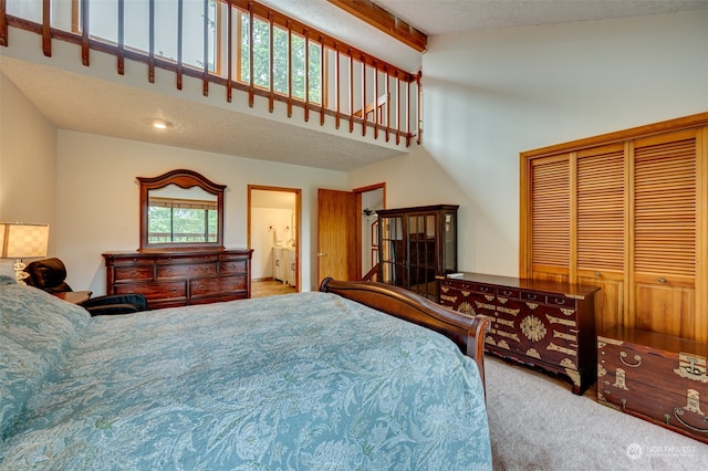 carpeted bedroom featuring a high ceiling, a textured ceiling, a closet, and ensuite bath