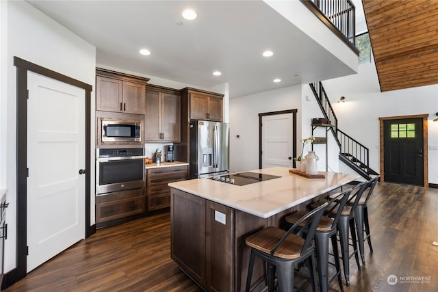 kitchen with dark hardwood / wood-style flooring, a kitchen island, stainless steel appliances, and dark brown cabinets