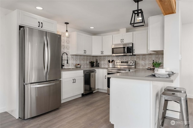 kitchen featuring kitchen peninsula, stainless steel appliances, decorative light fixtures, light hardwood / wood-style floors, and white cabinetry