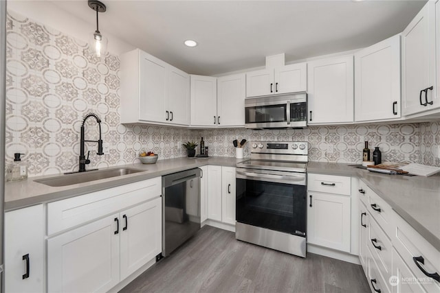 kitchen with sink, hanging light fixtures, light wood-type flooring, white cabinetry, and stainless steel appliances