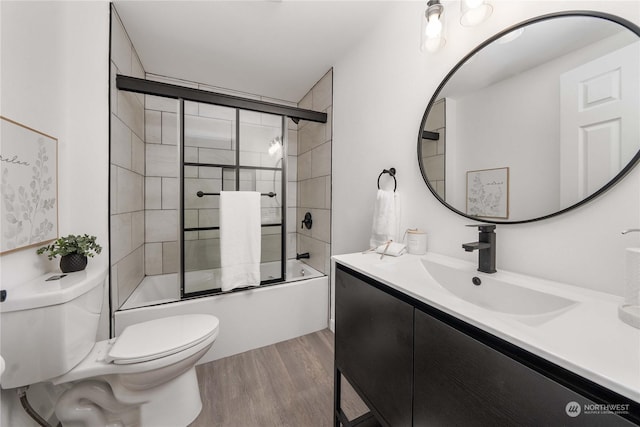 full bathroom with combined bath / shower with glass door, wood-type flooring, vanity, and toilet