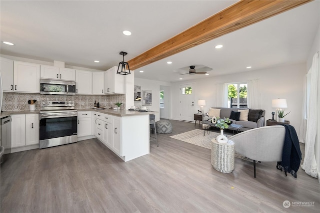 kitchen featuring beam ceiling, white cabinetry, stainless steel appliances, kitchen peninsula, and decorative light fixtures