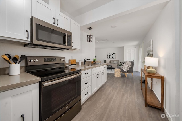 kitchen featuring white cabinets, light wood-type flooring, stainless steel appliances, and hanging light fixtures