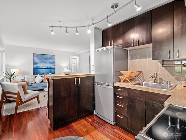 kitchen with stove, sink, dark hardwood / wood-style floors, tasteful backsplash, and stainless steel refrigerator