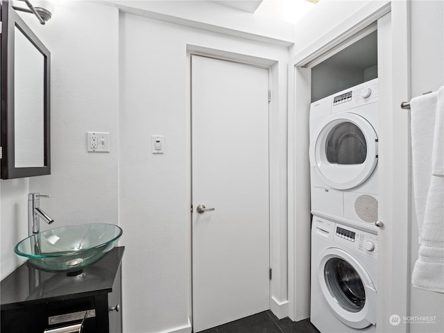 laundry area featuring sink, dark tile patterned floors, and stacked washer / dryer