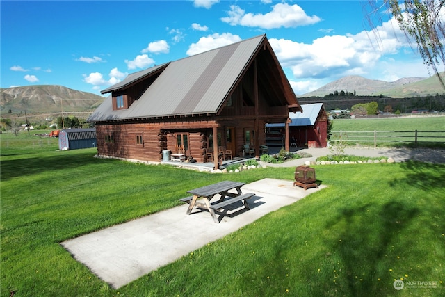 rear view of property with an outdoor structure, a patio area, a mountain view, and a lawn