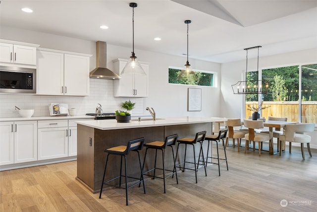 kitchen with a center island with sink, white cabinets, stainless steel appliances, and wall chimney range hood