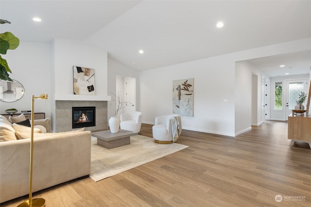 living room featuring a tiled fireplace, vaulted ceiling, and hardwood / wood-style flooring