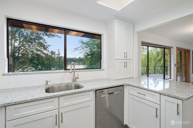 kitchen with a peninsula, a sink, decorative backsplash, white cabinets, and stainless steel dishwasher