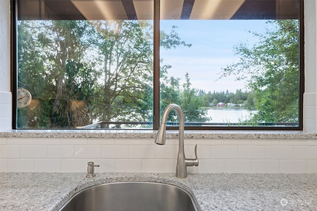 interior details with a sink, light stone counters, and a water view