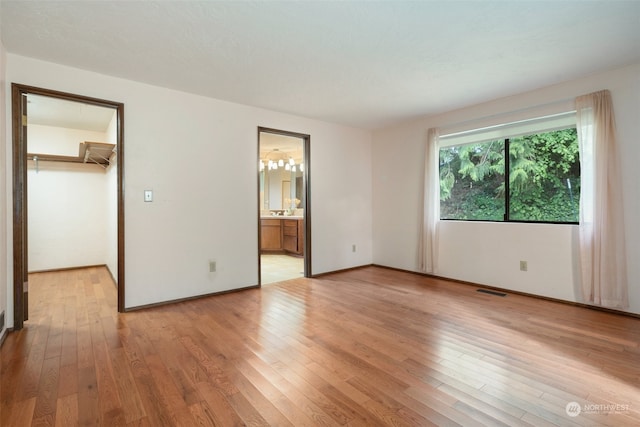 unfurnished bedroom featuring visible vents, a walk in closet, baseboards, light wood-style floors, and ensuite bath