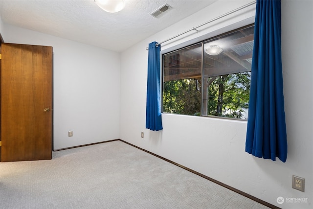 carpeted spare room with baseboards, visible vents, and a textured ceiling