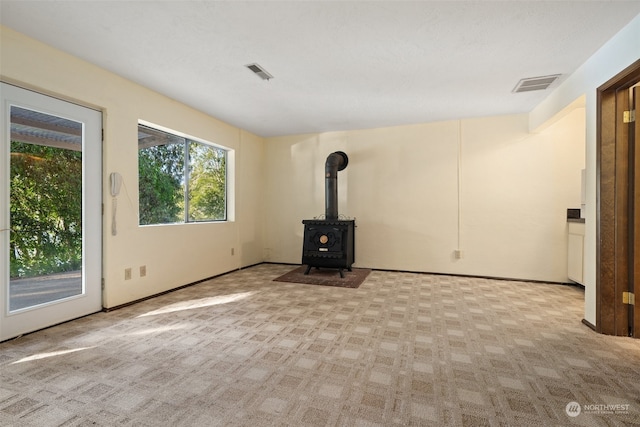 unfurnished living room featuring visible vents, light colored carpet, and a wood stove