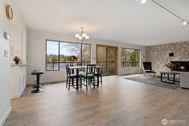 dining space featuring a stone fireplace, a notable chandelier, baseboards, and light wood-type flooring