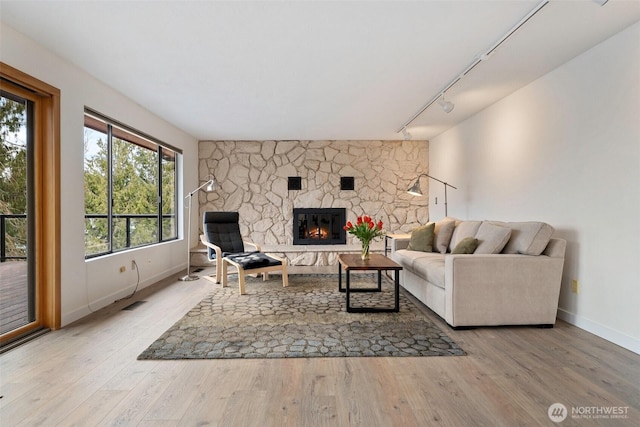 living area with a stone fireplace, track lighting, wood finished floors, and baseboards