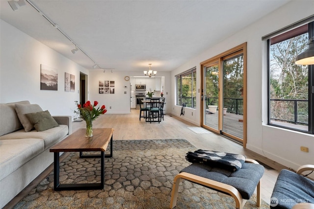 living room featuring a wealth of natural light, a chandelier, light wood-style flooring, and baseboards